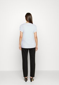 Light blue cotton t-shirt with rolled sleeves, relaxed fit, and a small logo detail on the back, paired with black straight-leg pants.