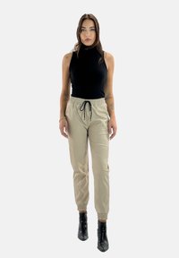 Top negro sin mangas combinado con pantalones jogger de un beige claro con una cinturilla y puños elásticos, acentuado con un detalle de cordón. Botas de tobillo negras.