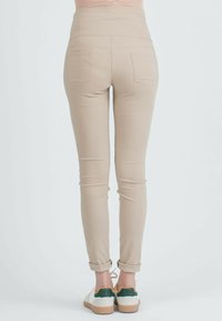 Beige hooggeprijsde broek met een slim fit, voorzien van twee achterzakken. Opgekrulde manchetten en gedragen met witte en groene schoenen. Soepele, rekbare stof.