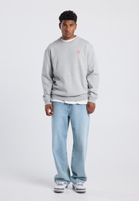 Gray sweatshirt with front logo, crew neck design, soft texture. Paired with light blue baggy jeans and white sneakers. Simple, casual look.