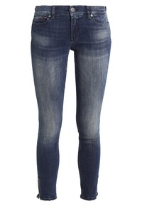 Jeans ajustados de denim azul oscuro, con un acabado desgastado, diseño clásico de cinco bolsillos, costuras claras y cremalleras en los tobillos.