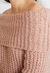 Rosa gestrickter Pullover mit weit geschnittenem Ausschnitt, Rippenstruktur und weichem, flauschigem Material. Das Design ist lässig mit einem schulterfreien Stil.
