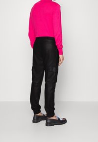 Zwarte cargo broek met zijzakken, elastische boorden, gecombineerd met een felroze languithemd. De schoenen hebben een grafisch ontwerp.