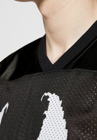 Black sports jersey with a mesh texture, featuring a V-neck and white graphic accents. The fabric appears lightweight and breathable.