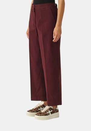 Pantaloni bordeaux a gamba larga con vita alta, caratterizzati da pieghe anteriori e dettagli in metallo; abbinati a sneakers con stampa leopardata e suole bianche.