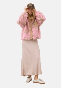 Roze en beige fuzzy jas met een beige knoopsluiting, gedragen over een lange lichtroze rok en witte sneakers met bruine accenten.