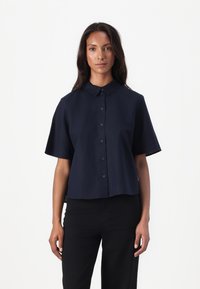 Marine kortermet skjorte med knapper, med klassisk krage, lett cropped design og jevn tekstur. Komplimentert med mørke bukser.