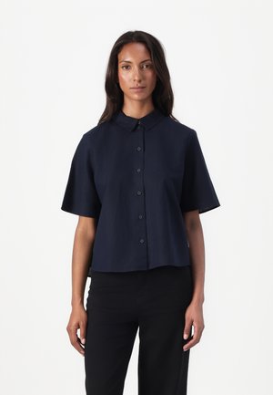 Marineblaues Kurzarm-Hemd mit Knöpfen, das einen klassischen Kragen, ein leicht verkürztes Design und eine glatte Textur aufweist. Ergänzt durch dunkle Hosen.