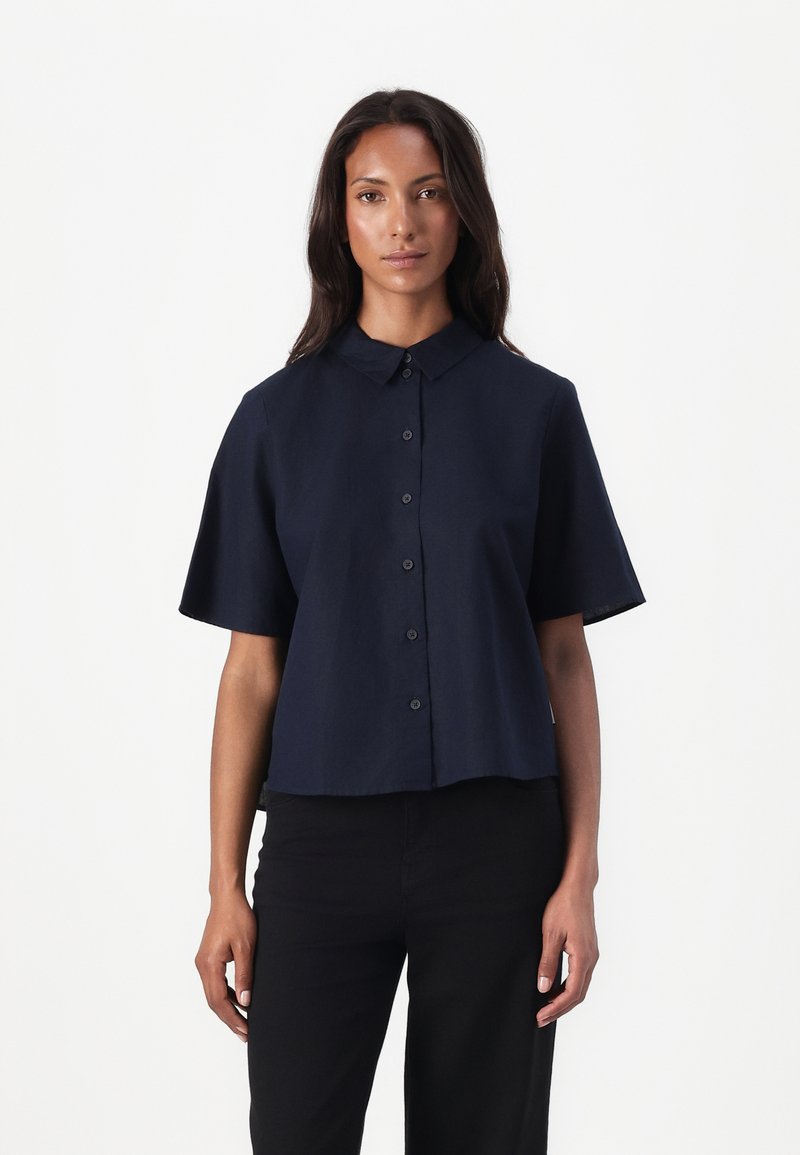 Marine kortermet skjorte med knapper, med klassisk krage, lett cropped design og jevn tekstur. Komplimentert med mørke bukser.