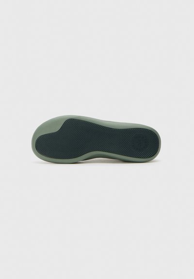 Shoe outsole in dark green with a textured rubber surface. Features a rounded shape and a circular logo embossed on the side.