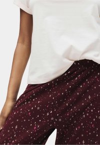 Camiseta blanca con mangas enrolladas combinada con pantalones burdeos de estampado con estrellas y lunas en tonos rosa, blanco y dorado.