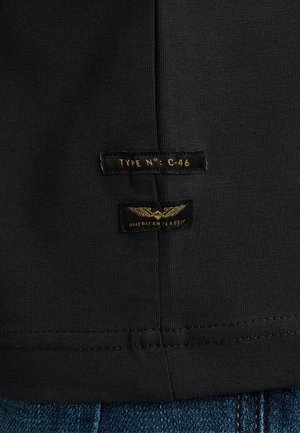 Sort bomulds t-shirt med to labels: "TYPE N°: C-46" og "AMERICAN CLASSIC," med guld tekst og vinge grafik. Syet kantdetalje.