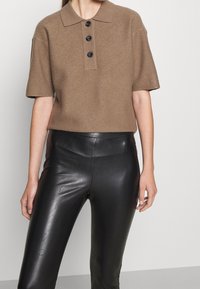 Brun kortärmad polo-liknande topp i texturerat tyg, med en femknapplång placket och en avslappnad passform, kombinerad med svarta läderbyxor.