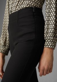 Zwarte high-waisted broek met een gladde textuur en zijzakken; gedragen met een gestreept shirt met geometrische ontwerpen in beige en zwart.