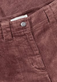 Kostymbyxor i djup mauve, med ribbad textur, framficka och knappstängning. Etikett med storlek 36 synlig vid midjan.