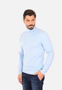 Maglione a collo alto blu chiaro con vestibilità slim, polsini e orlo a coste. Indossato con jeans blu scuro, che mostrano una consistenza liscia e morbida.