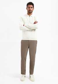 Crème pullover met rits en kraag, gecombineerd met lichtbruine broek en witte sneakers. Gladde texturen, moderne pasvorm, neutrale kleuren.