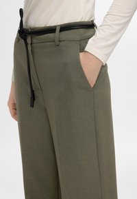 Õlivihmrohelised püksid sileda tekstuuriga, millel on must nöörvöö, küljetaskud ja liibuv lõige.