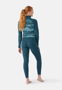 Maglione termico teal con maniche lunghe e colletto alto, caratterizzato da un motivo ondulato sul retro, abbinato a leggings aderenti coordinati.