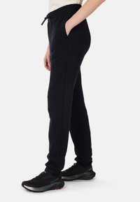 Zwarte joggerbroeken met elastische tailleband, zijzakken, taps toelopende benen en een gladde textuur, gecombineerd met zwarte sportschoenen.