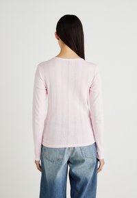Haut en tricot à côtes roses à manches longues avec un col arrondi et un motif texturé vertical. Associé à un jean en denim bleu clair taille haute.