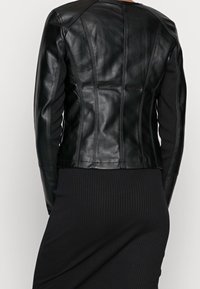 Zwarte leren jas met een aansluitend ontwerp, voorzien van verticale naden, lange mouwen en een cropped zoom, gecombineerd met een geribbelde zwarte rok.