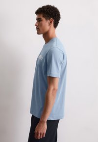 Lichtblauwe katoenen t-shirt met korte mouwen en een ronde halslijn. Heeft een bedrukte logo-ontwerp aan de voorkant. Regular fit.