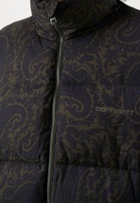 Gilet scuro con motivo paisley in viola su uno sfondo nero, dotato di un colletto alto e una zip frontale.