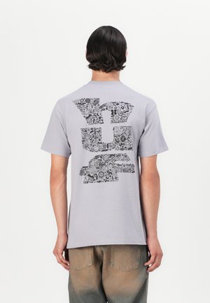 Kortærmet grå t-shirt med et stort sort abstrakt design på ryggen, lavet af blødt stof med en afslappet pasform.