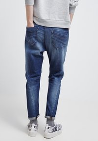 Tummansiniset farkut, joissa on kapeneva malli, kahdella takataskulla ja lievästi haalistunut pinta. Yhdistetty vaaleanharmaisiin ja kuvioituihin lenkkareihin.