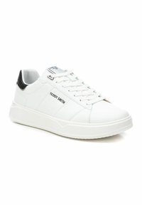Zapatilla de cuero blanca con un acabado suave, lengüeta acolchada y acento negro en el talón. Presenta una suela de goma texturizada y un diseño de cordones ocultos.