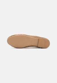 Ljust brunt vävt espadrille med en platt gummisula, med en mjuk yta och präglad logotyp på undersidan.