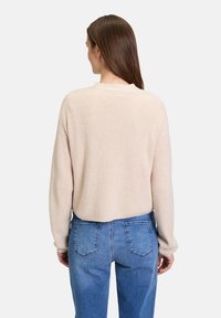 Beiger, gerippter Pullover mit langen Ärmeln und lockerer Passform, kombiniert mit hellblauen Jeans. Einfaches Design, keine sichtbaren Muster oder Akzente.