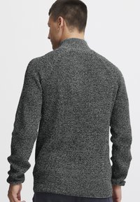 Gestrickter Pullover in Grau und Schwarz mit einer strukturierten Oberfläche. Verfügt über lange Ärmel und einen hohen Kragen. Einfaches Design ohne sichtbare Muster oder Akzente.