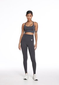 Czarny sportowy stanik w ciemnoszarym kolorze z cienkimi ramiączkami oraz dopasowane legginsy z wysokim stanem, z małym logo na pasku. Białe sneakersy dopełniają całość.