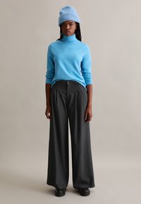 Lichtblauwe coltrui, grijze wijde broek en een blauwe gebreide muts. De stof lijkt zacht met een gladde textuur.