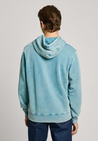 Lichtblauwe hoodie met verstelbare trekkoordkap, ribgebreide manchetten en zoom. Zachte textuur met een lichte schaduwtint op de stof.