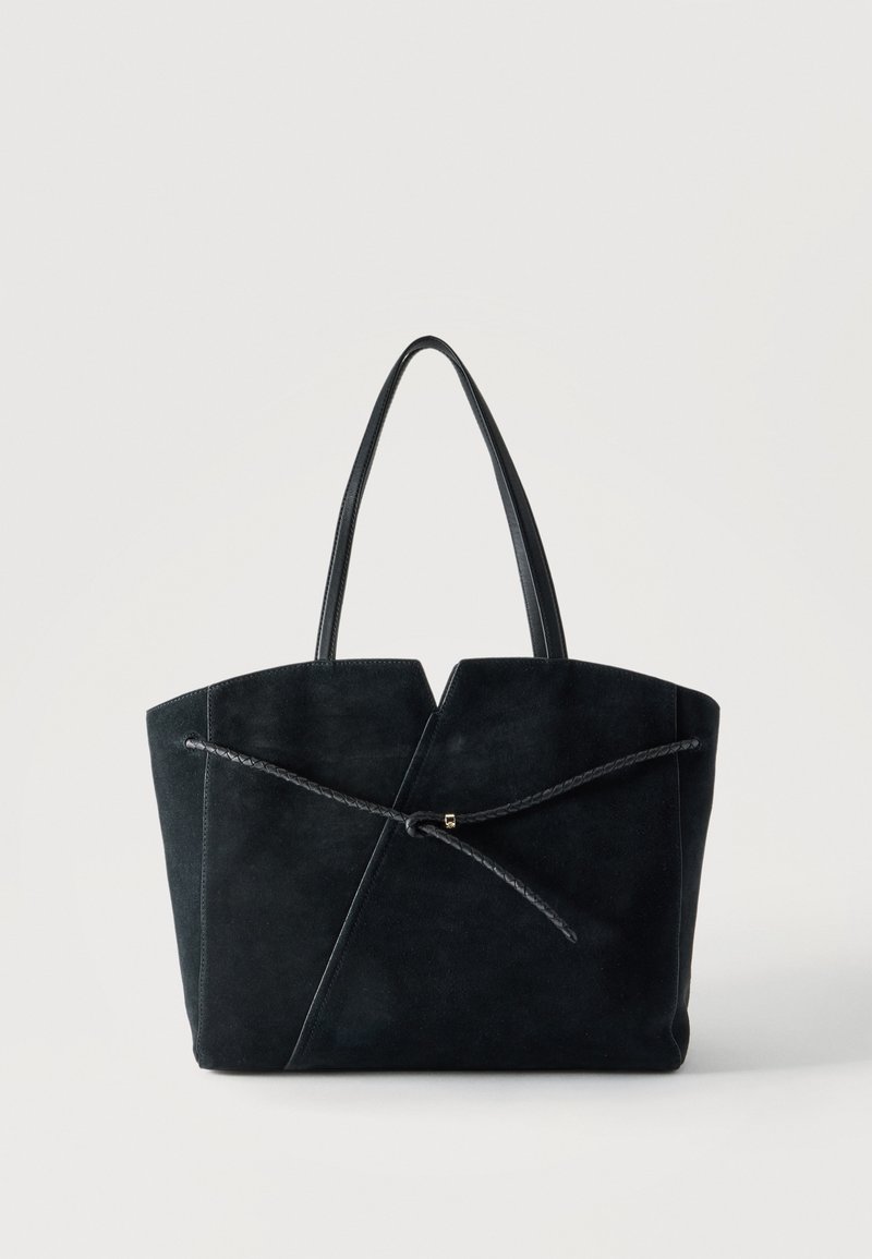 Sac cabas en daim noir avec deux fines poignées en cuir et un cordon en cuir tressé noué à l'avant.