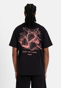 Camiseta de algodón negra con una gran ilustración de fresa rosa y el texto "DISFRUTA DEL SABOR" en la parte posterior. Corte estándar con mangas cortas.