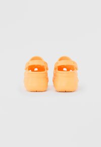 Sabots en caoutchouc orange avec une sangle à l'arrière, présentant des trous de ventilation sur les côtés, une surface extérieure texturée et une semelle plate.