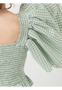 Grön och vit rutmönstrad blus med puffärmar, smockad byst och fyrkantig halsringning. Tyget har en mjuk, lätt textur.