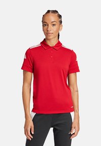 Polo shirt rosso con colletto, maniche corte, patta con tre bottoni e strisce bianche sulle spalle. Realizzato in tessuto liscio e traspirante.
