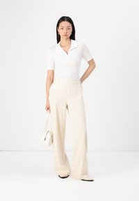 Vit kortärmad polo skjorta kombinerad med högmidjade krämfärgade vida byxor. Accessoarer med en liten vit handväska och svarta ballerinas.
