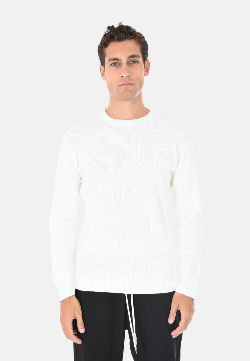 Maglione bianco a coste con scollatura tonda e maniche lunghe, abbinato a pantaloni neri con cordino, caratterizzati da un design a maglia testurizzata.