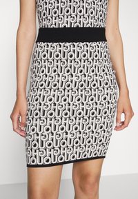 Jupe bodycon à motifs noir et blanc présentant un design de logo géométrique, avec une taille cintrée noire et un tissu lisse et texturé.