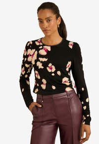 Garais piedurkņu melnais krekls ar rozā un bēša leoparda rakstu, ar apaļu izgriezumu un pieguļošu formu, apvienots ar augsto vidukli bordo ādas biksēm.