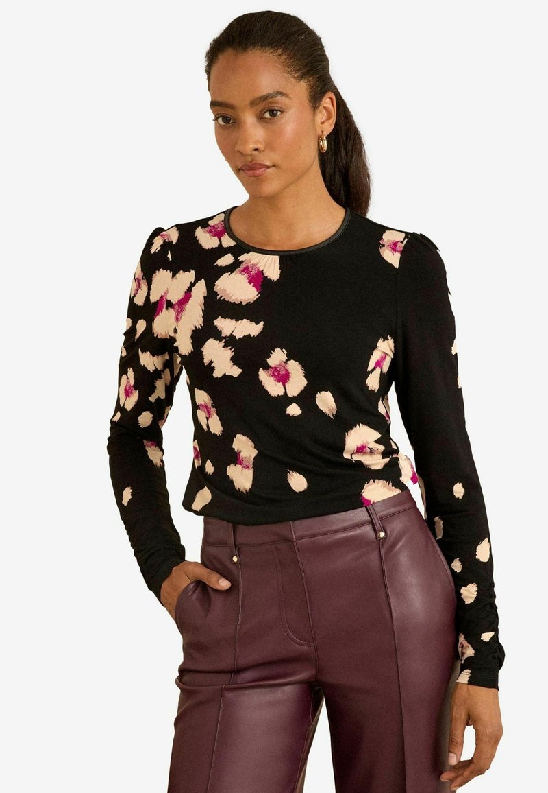 Garais piedurkņu melnais krekls ar rozā un bēša leoparda rakstu, ar apaļu izgriezumu un pieguļošu formu, apvienots ar augsto vidukli bordo ādas biksēm.