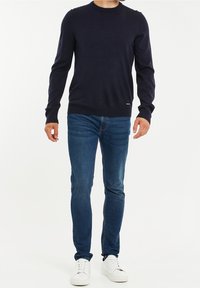 Pull en maille bleu marine avec col rond, manches longues et poignets côtelés ; associé à un jean denim ajusté et des baskets blanches.
