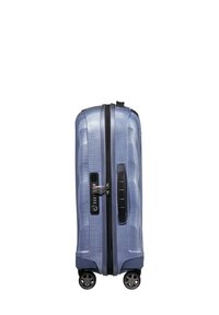 Hard-shell suitcase in grayish-blue with a textured surface, black zipper, locking mechanism, and four wheels for mobility.