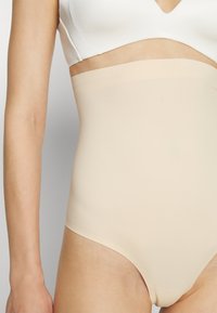 Nude visoke gaćice izrađene od glatke tkanine, s bešavnim dizajnom, širokim pojasom i standardnim otvorima za noge.